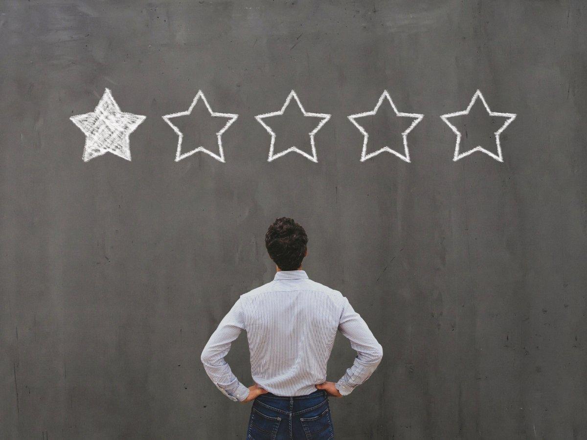 Person stands with hands on hips, facing a chalkboard with five chalk stars across the top; the first star is filled.