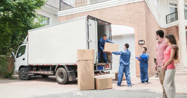 three movers moving boxes out of a moving truck while a couple watches