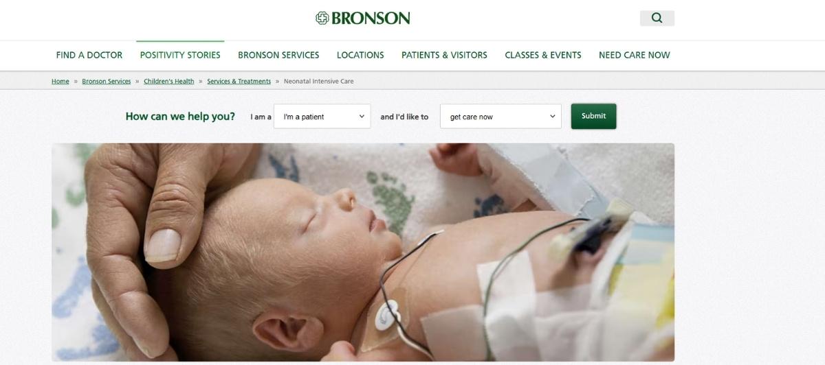 Close-up of a newborn baby lying in a hospital bed with medical sensors and tape on the chest, and a caregiver's hand gently cradling the baby's head.