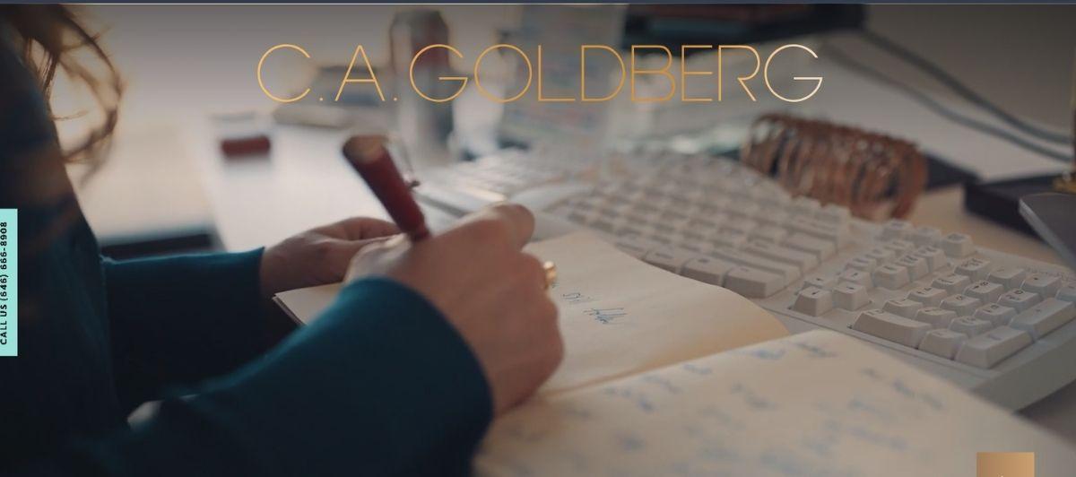 Professional desk scene with a person writing in a notebook beside a computer keyboard and a gold-toned 'C.A. GOLDBERG' banner across the top; a vertical 'Call Us' label on the left edge.