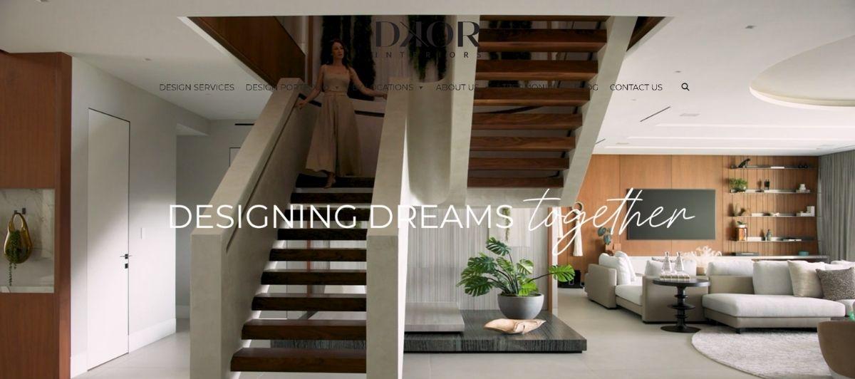 Open-concept living room with a floating wooden staircase, white walls, and a gray sofa; overlay text reads 'DESIGNING DREAMS together'.