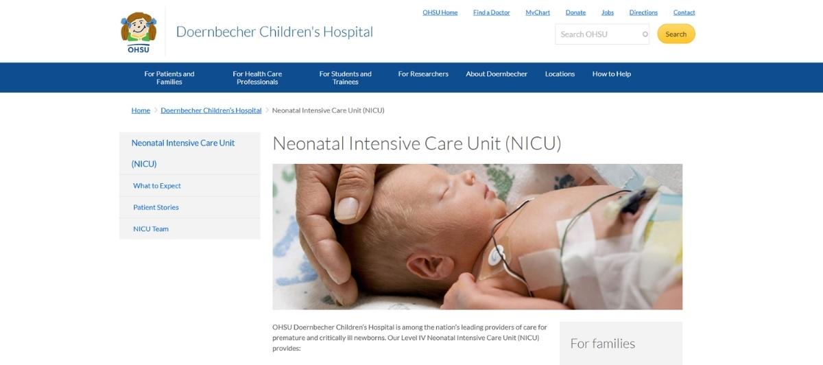 Newborn baby in NICU with medical sensors attached, held by an adult hand.