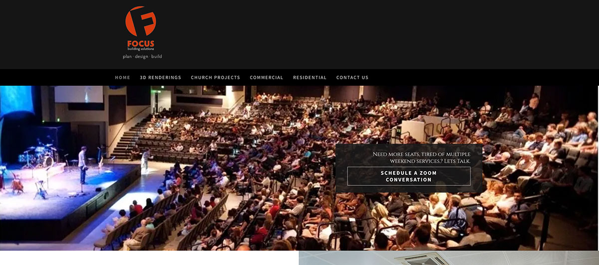 Wide shot of a packed auditorium with a stage on the left and audience seated in rows under a dark header with a logo above.