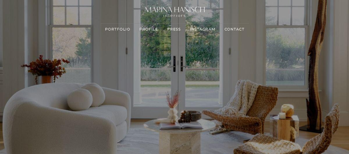 Hero image for Marina Hanish Interiors showing a bright living room with a white curved sofa, woven lounge chairs, and large glass doors behind, with branding text overlaid.