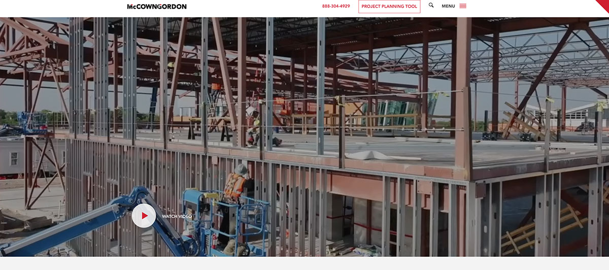 Construction site with steel framing and workers on an upper level; a play button reads 'Watch Video' in the lower left corner.