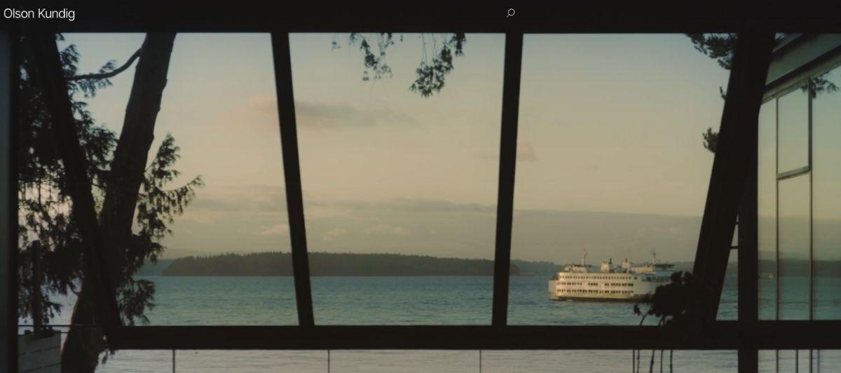 Water view through large window frames; distant forested shore and a white passenger ferry on the right.