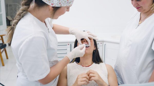 Dentist and assistant in white coats with gloves placing a dental appliance on the patient’s teeth in a bright clinic.