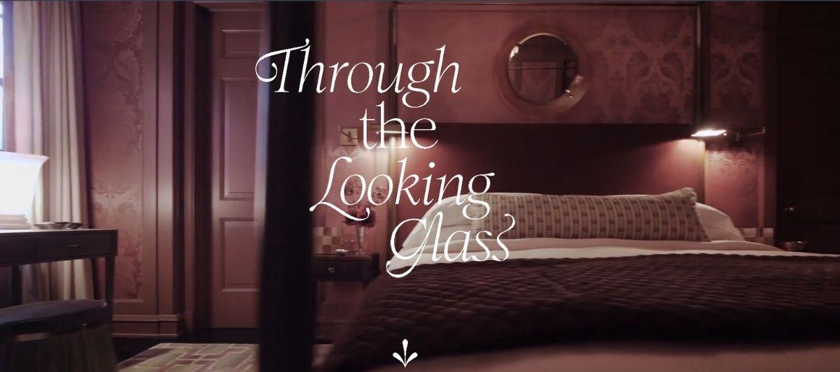 Dimly lit hotel-style bedroom with a four-poster bed, burgundy walls, and warm lamps; the title 'Through the Looking Glass' appears in elegant white cursive text over the center.