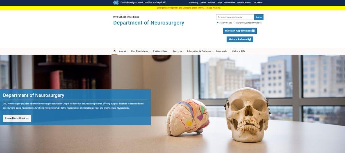 Hero image for UNC Department of Neurosurgery showing skull and brain models on a desk with a city view through large windows, conveying neurosurgery focus.