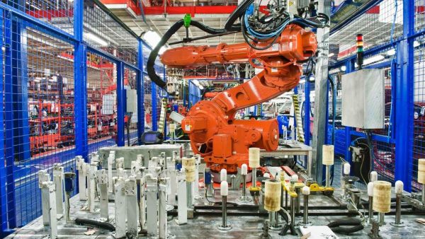 Orange industrial robotic arm operating inside a blue safety-fenced production cell in a factory setting.Good for automated manufacturing.