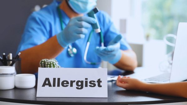 Allergist at a clinic desk showing a sign that reads 'Allergist' during a patient consultation with medical tools nearby