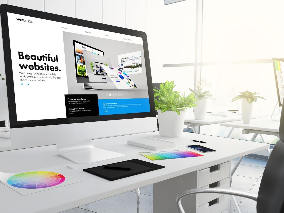 White desktop with a large monitor displaying a web design page and the words "Beautiful websites" beside color swatches and a color wheel on the desk.