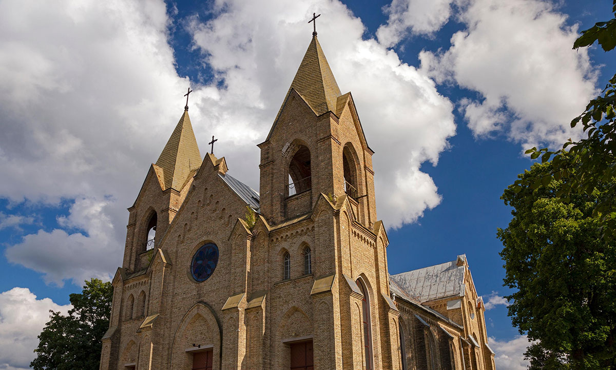 Brick church with twin steeples reaching toward a blue sky with white clouds.
