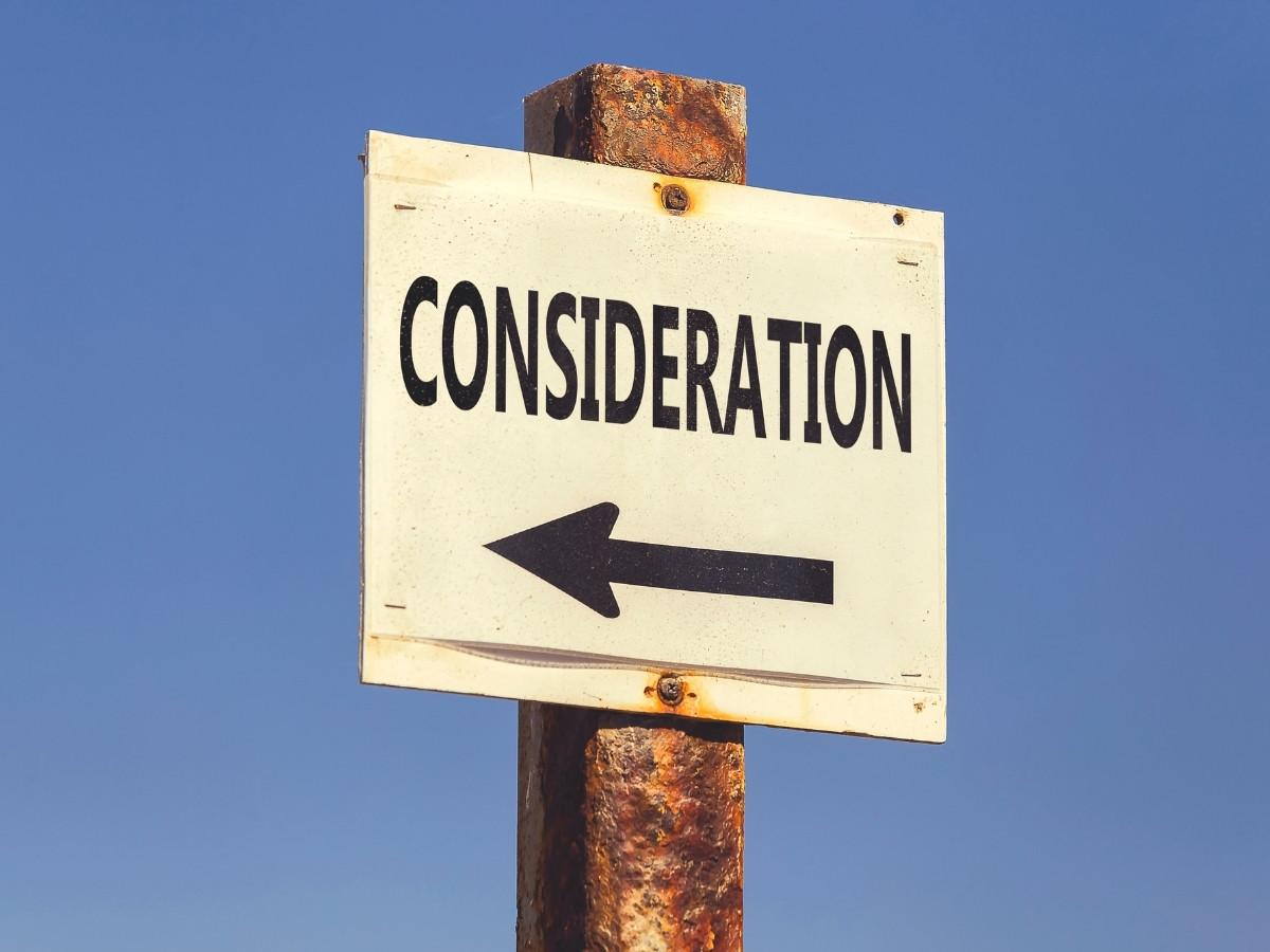 Sign reading 'CONSIDERATION' with a left-pointing arrow mounted on a rusted post against a clear blue sky.
