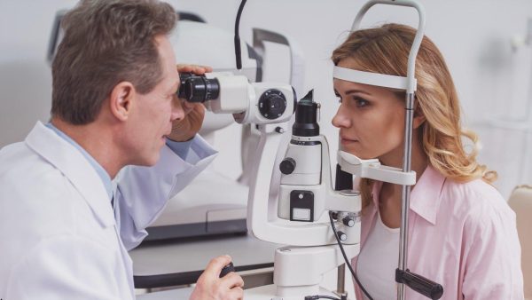 Ophthalmologist adjusts a slit lamp as a woman undergoes an eye exam.
