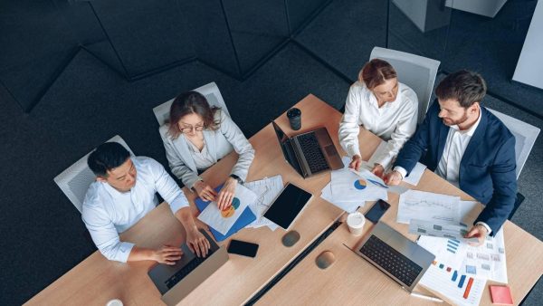 Overhead view of four professionals around a table examining charts and graphs on paper and laptops.