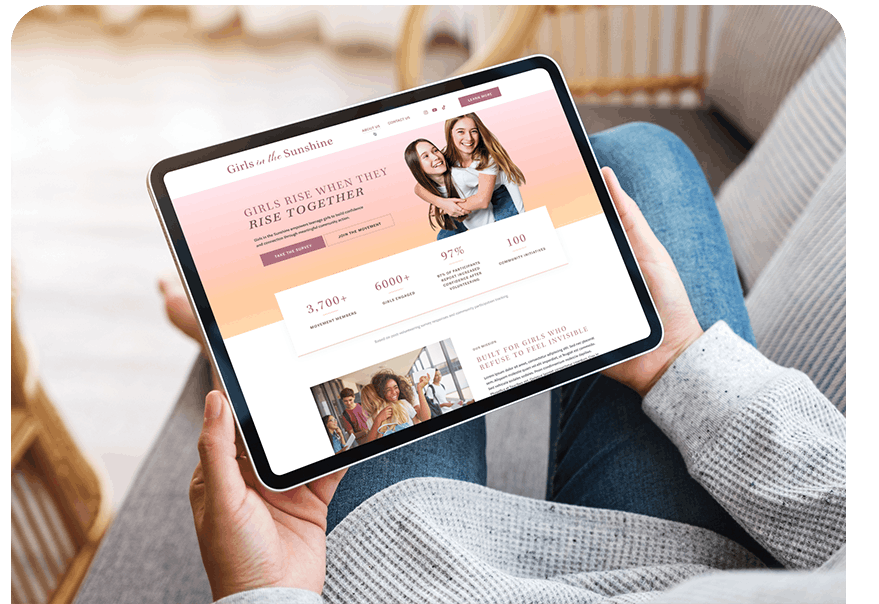Tablet on a person’s lap showing a charity website about girls’ empowerment, with a photo of two smiling girls on the screen.