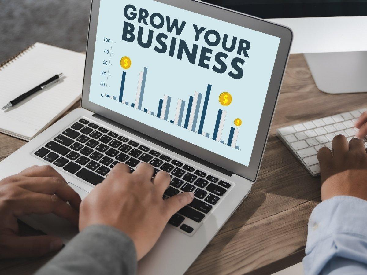 Laptop screen shows a 'GROW YOUR BUSINESS' graphic with a bar chart and coin icons, indicating growth prospects.
