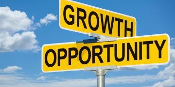 Yellow street signs intersecting read 'GROWTH' and 'OPPORTUNITY' against a blue sky, suggesting business growth.