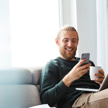 Man excitedly looking at phone and laptop