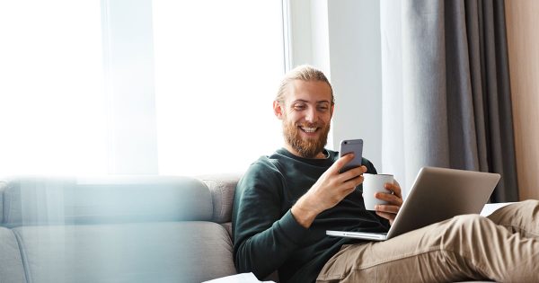 Man excitedly looking at phone and laptop