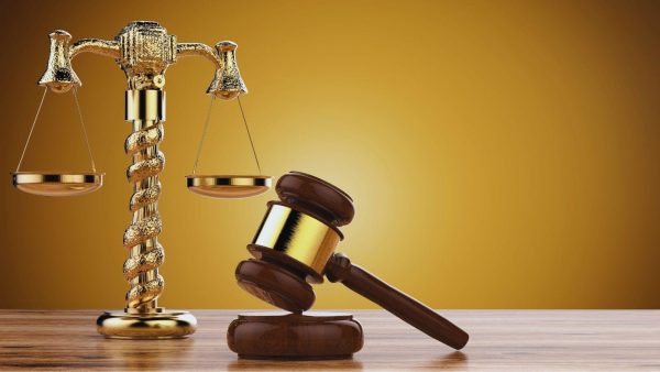 Gold judge's scales and a gavel on a wooden table, symbolizing justice in a warm background