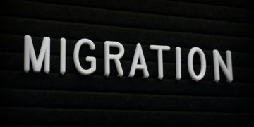 White 3D letters spell the word MIGRATION on a dark, ribbed background.