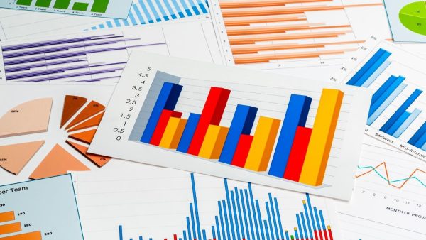 Assortment of business charts and graphs on a desk, including multicolored bar chart, pie slices, and line/bar graphs.