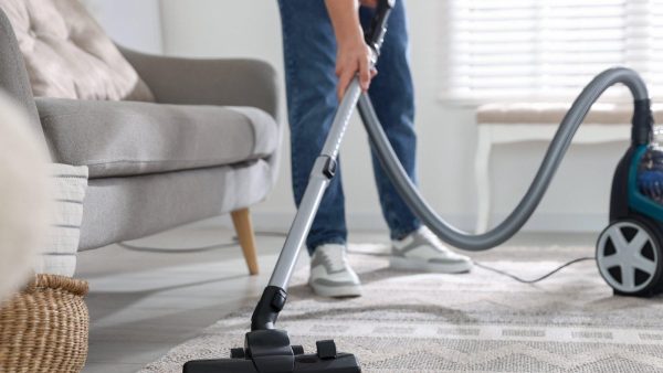 Person vacuuming a living room rug with a canister vacuum and hose in a bright, modern space.