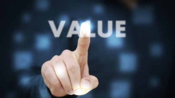 Close-up of a hand with the index finger pointing at a glowing word 'VALUE' against a dark, blurred background.