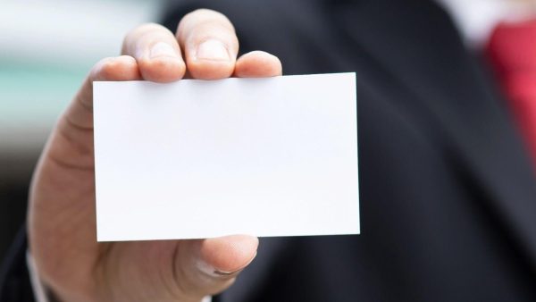 Close-up of a hand holding a blank white business card against a dark suit background.