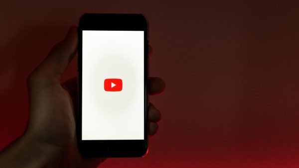 Hand holding a smartphone displaying the YouTube app logo on a white screen.