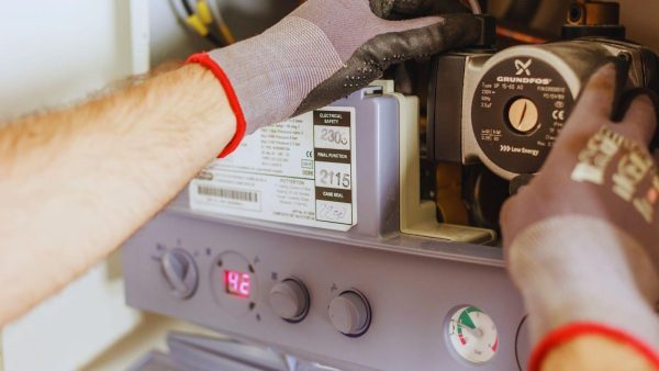 HVAC technician wearing gloves servicing a boiler, adjusting the pump and control panel