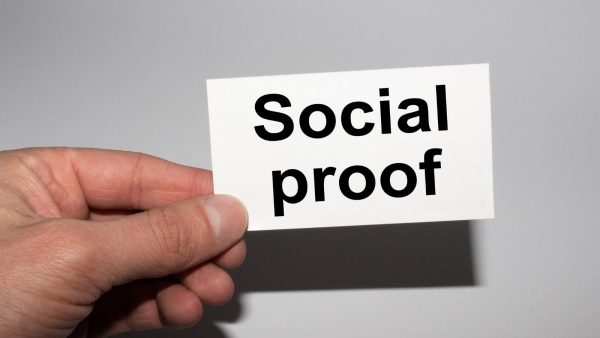 Hand holding a white card with the bold words 'Social proof' on a gray background