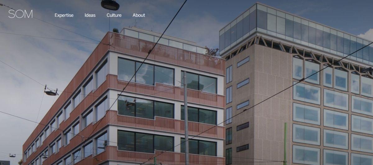 Modern multi-story glass-and-brick office building with overhead cables; SOM website header is visible in the top left.