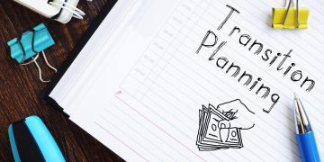 Notebook page reads 'Transcript Planning' with a sketch of a hand holding cash, surrounded by binder clips, a pen, and other desk supplies on a wooden surface