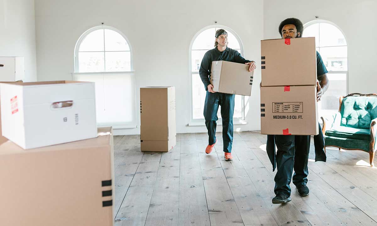 two movers moving boxes in a room