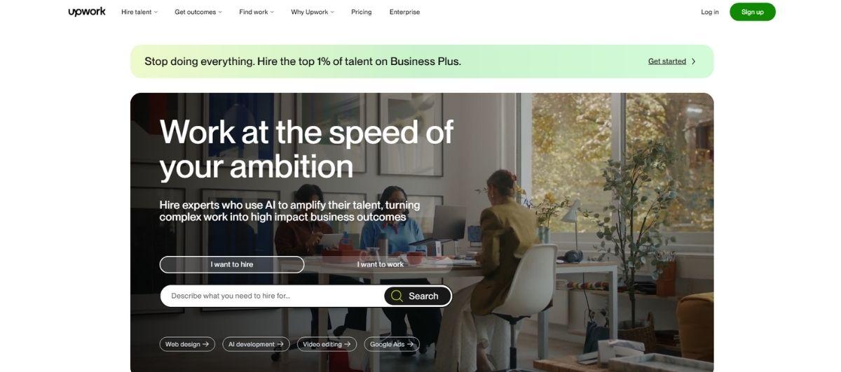 Upwork homepage hero: a modern office scene with people at a table, large text 'Work at the speed of your ambition' overlaid, plus a search bar and two role options (I want to hire / I want to work).