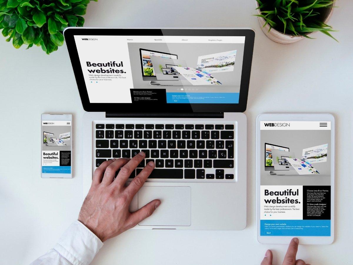 Laptop, tablet, and smartphone on a white desk displaying a web design with the phrase 'Beautiful websites'.