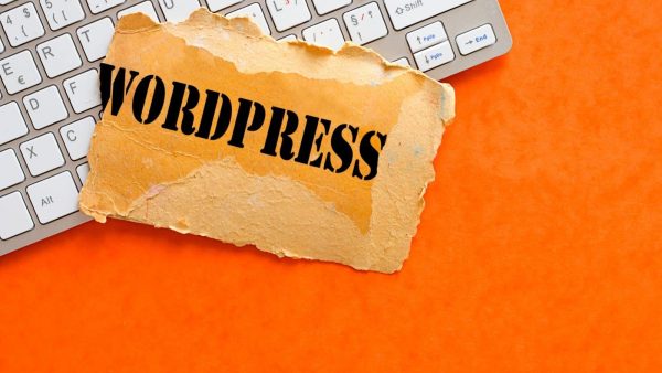 Torn piece of paper with the word WORDPRESS in bold black letters on an orange background near a computer keyboard.