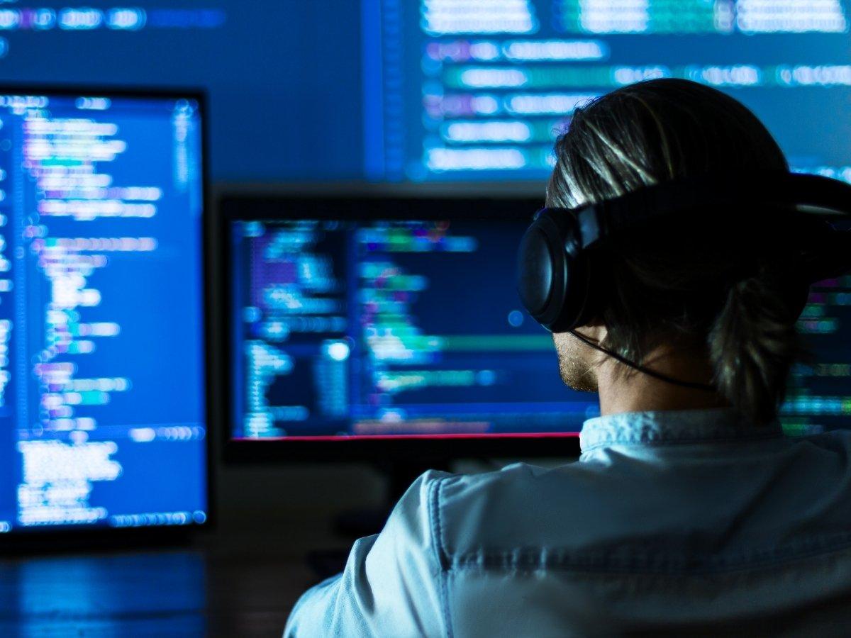 Person wearing a headset, seated at a desk with multiple monitors displaying code and blue glow.
